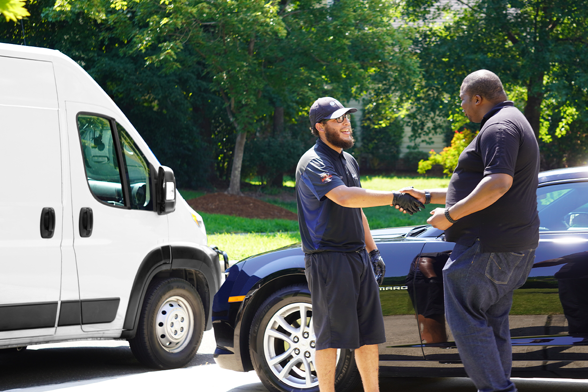 Mobile service technician shaking hands with a customer in a driveway beside a Spiffy service van