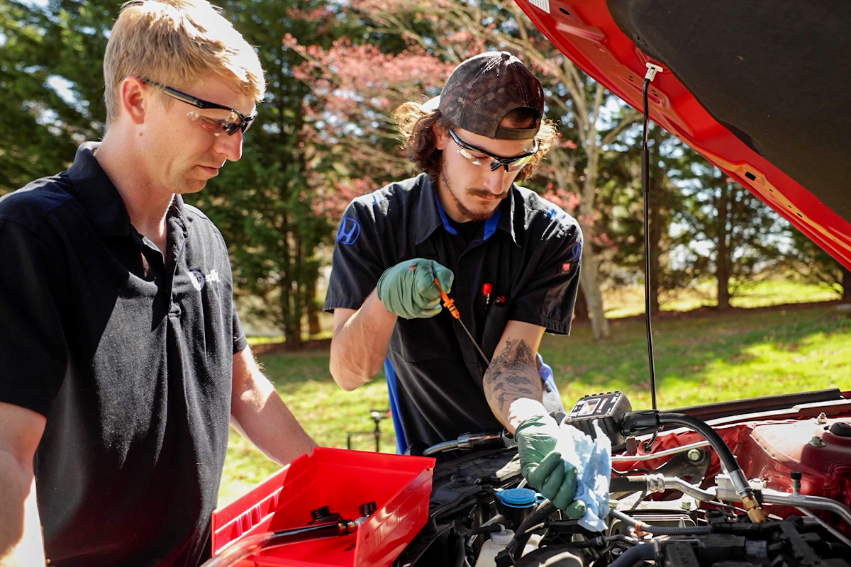 Experienced technician training a newer mobile technician at the engine bay of a vehicle on site