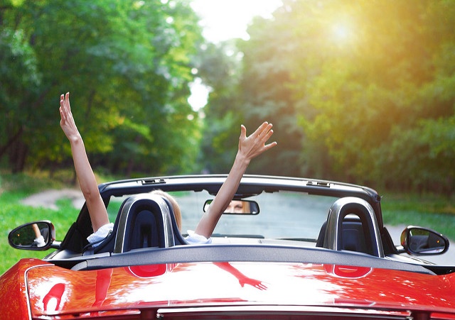 Independent woman lifting her arms excitedly in a red convertible